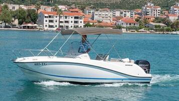 A speedboat with a cabin and a motor, moving on a body of water with a coastal town in the background.
