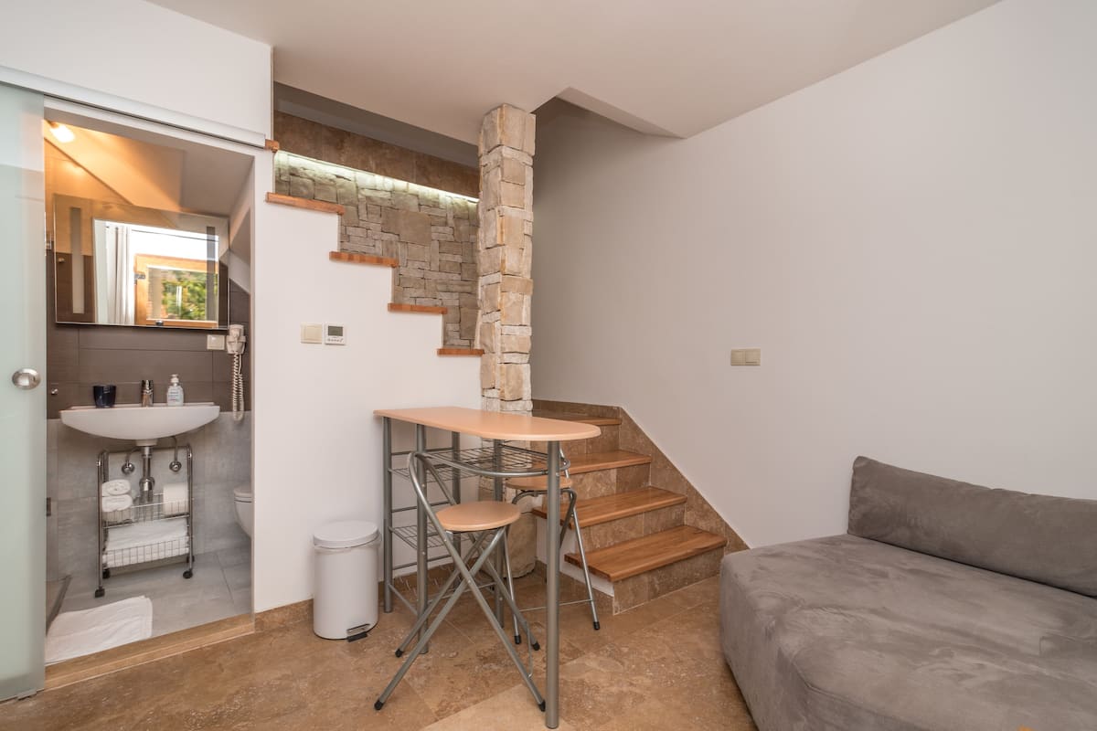 A compact living space with a kitchenette, a small dining table, a sofa, and a stone accent wall.