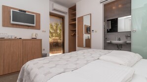 A modern bedroom with a TV mounted on the wall, a wardrobe, a bedside table with a lamp, and a bathroom with a sink and mirror. - Villa Lucica Trogir (Trogir)