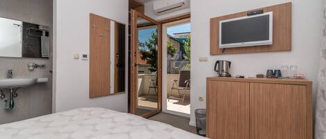 A modern hotel room with a bed, a wooden wardrobe, a television mounted on the wall, a sink, and an open door leading to a balcony.