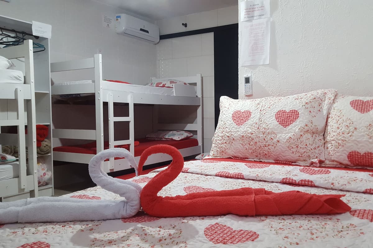 Un lit superposé avec une échelle, une armoire blanche et un lit avec une literie à motifs de cœurs.