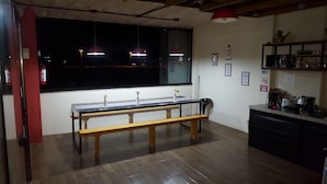 A kitchen with a wooden bench, a window with city lights visible, and various kitchen appliances. - Pousada Dois Corações (Penha)