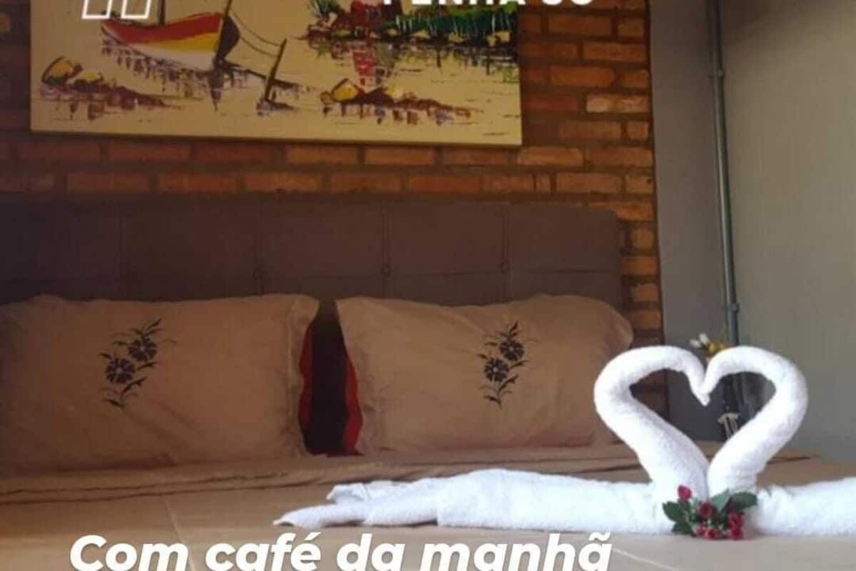 Une chambre d’hôtel avec un lit, des oreillers, une décoration en forme de cœur faite avec une serviette et un tableau au mur.