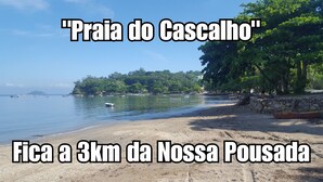 A beach with boats, a stone wall, and trees. - Pousada Dois Corações (Penha)