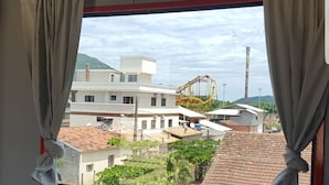 A room with a window overlooking a residential area, featuring a view of houses and a roller coaster. - Pousada Dois Corações (Penha)