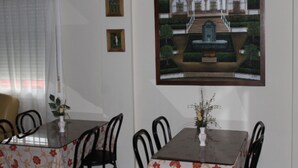Een eetgedeelte met een tafel, stoelen, een raam met gordijn en een lijst met foto.