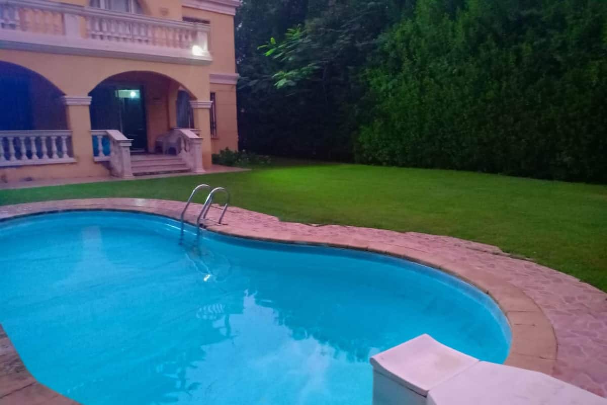 A swimming pool with a stone border, a small deck area, and a well-maintained lawn.