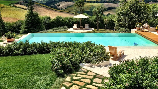 A swimming pool with a patio area, surrounded by lush greenery and hills in the background.