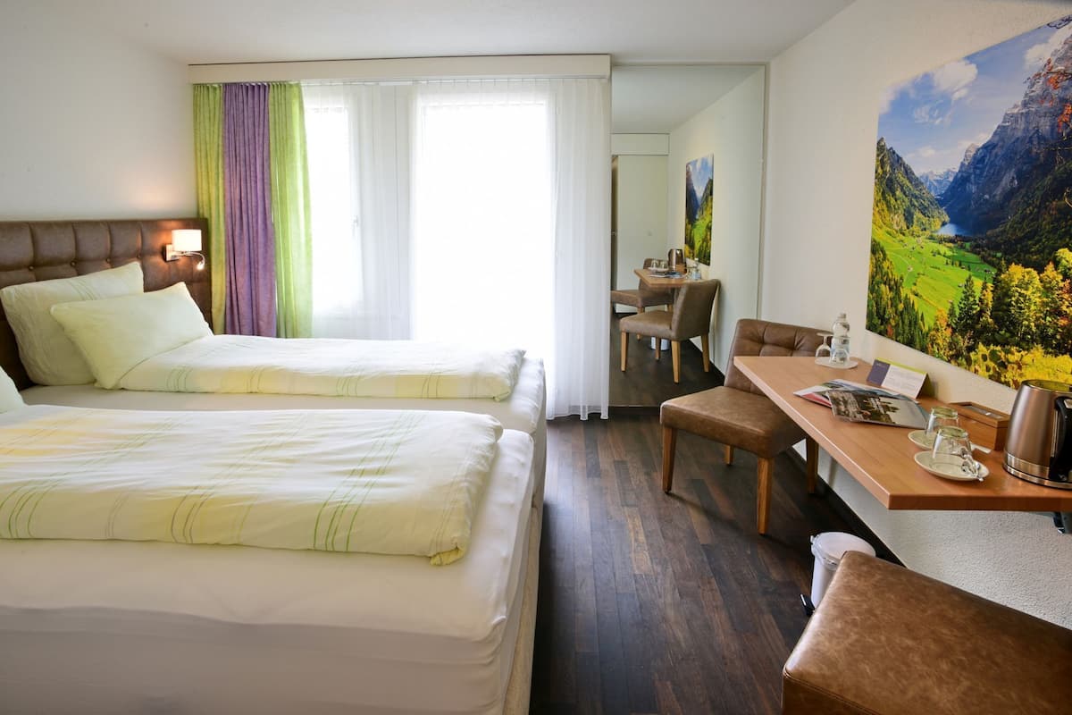 A hotel room with two beds, a dining area, and a painting of a mountain landscape.