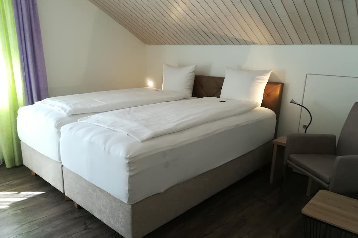 A double bed with white bedding, a bedside table, a chair, and a lamp.