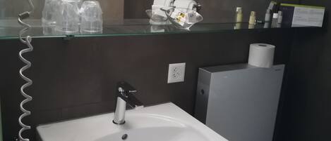 A bathroom with a white sink, a toilet, and a glass shelf above the sink holding toiletries.