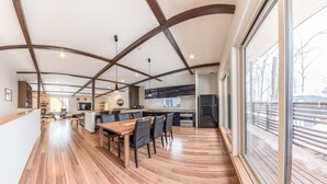 Una cocina amplia con una isla central, un comedor con mesa y sillas de madera, y ventanas grandes con vistas al exterior.