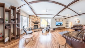 Un salón espacioso con chimenea de piedra, sofás de cuero, suelo de madera y estanterías empotradas con diversos objetos.