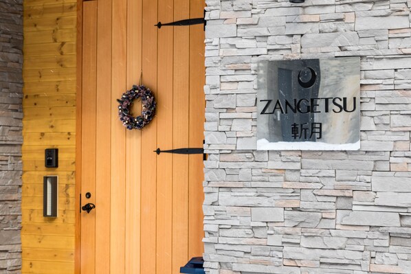 A wooden door with a wreath, a stone wall, and a sign reading "ZANGETSU".