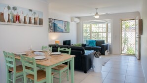 A dining area with a wooden table and chairs, a black sofa, and a painting on the wall. - Gold Coast Theme Park Villa (Coomera)