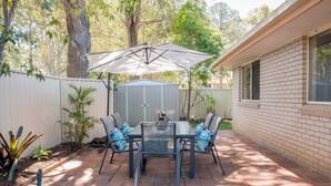 A patio with a table and chairs, an umbrella, and a shed in a backyard. - Gold Coast Theme Park Villa (Coomera)