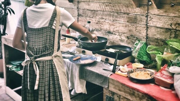 A rustic kitchen with wooden shelves, a hanging pot rack, and a variety of cooking utensils and ingredients on the counter. - Nego Home (Bangkok)
