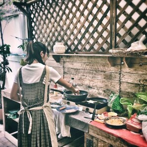 A rustic kitchen with wooden shelves, a hanging pot rack, and a variety of cooking utensils and ingredients on the counter. - Nego Home (Bangkok)