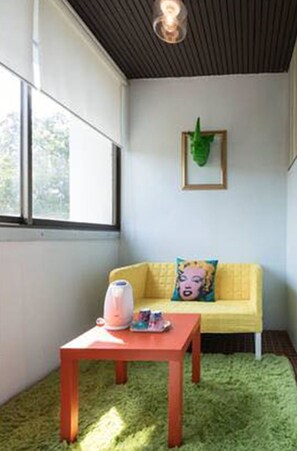 A room with a yellow sofa, a small table with a pink object, and a green rug. - Nego Home (Bangkok)