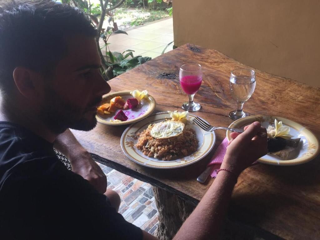 A person dining at a wooden table with plates of food and a glass of pink drink.