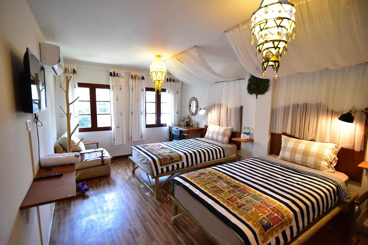 A hotel room with two beds, a desk, a chair, a TV, and a chandelier.
