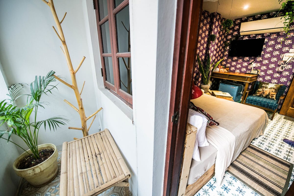 A room with a bed, a small table, a potted plant, and a TV on the wall.