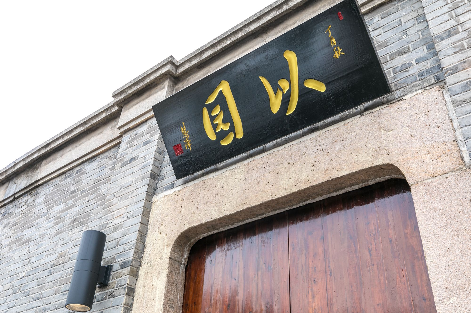 A building with a black sign with yellow characters and a wooden door.