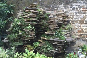 A rock garden with various plants and a brick wall in the background. - Memory of Pan＇s (Guilin)