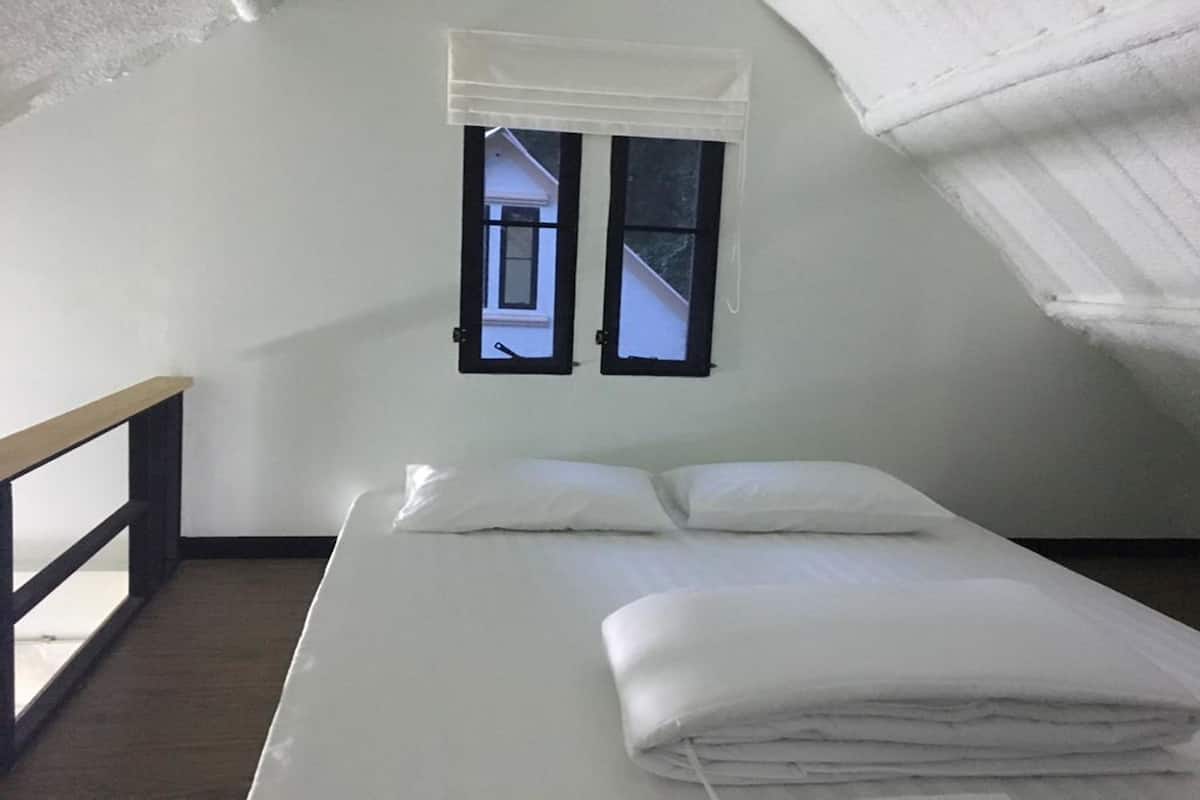 Een kleine kamer met een enkel bed, schuine wand en een raam met een witte zonwering.