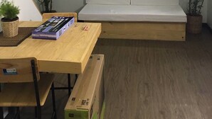 Een kleine kamer met een houten tafel, een witte bank en twee potplanten.