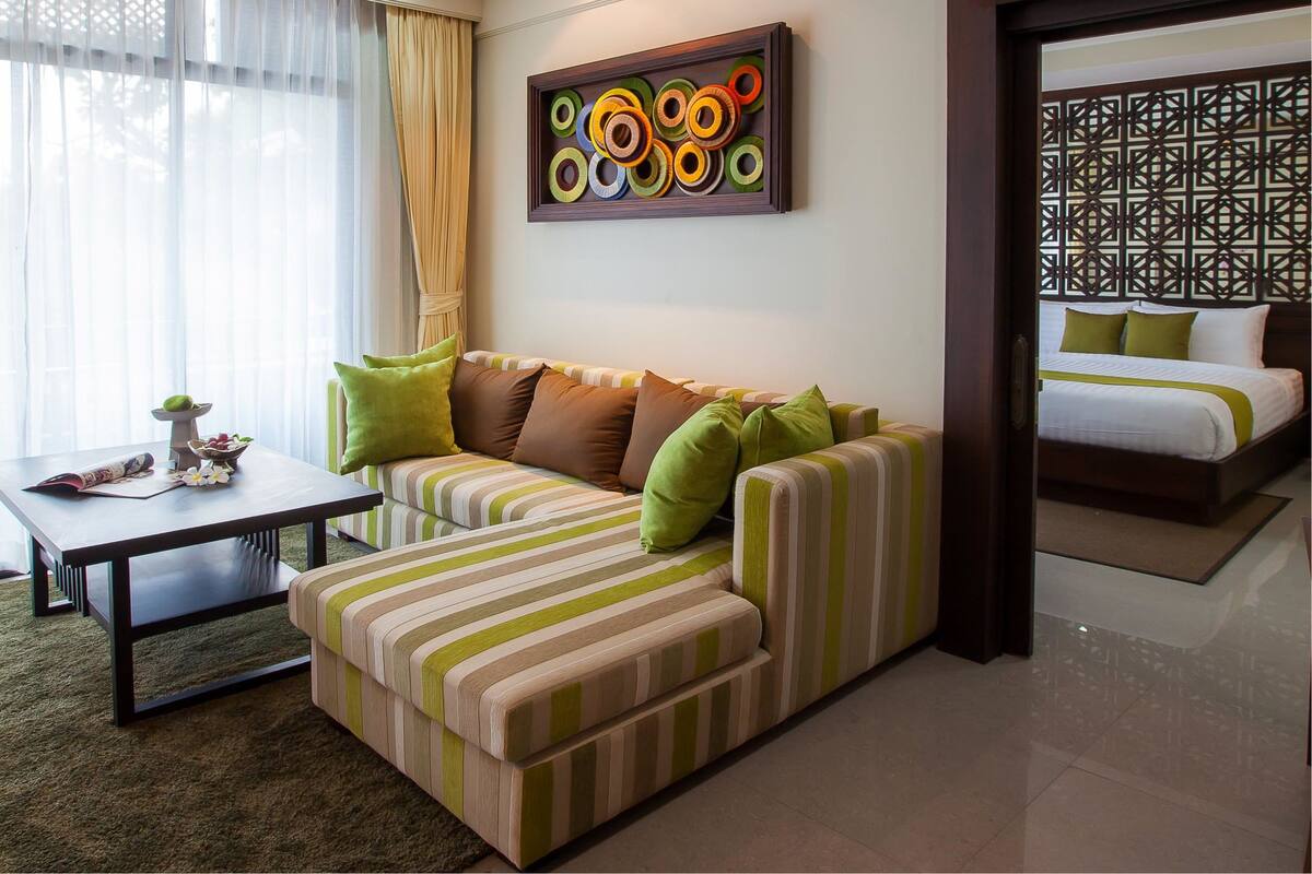 Habitación de hotel moderna con un sofá a rayas, una pequeña mesa con un florero y una cama con cabecera geométrica.