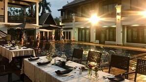 A dining area with tables set for a meal, overlooking a swimming pool, with a building in the background. - Huern Na Na Boutique Hotel (Phrae)