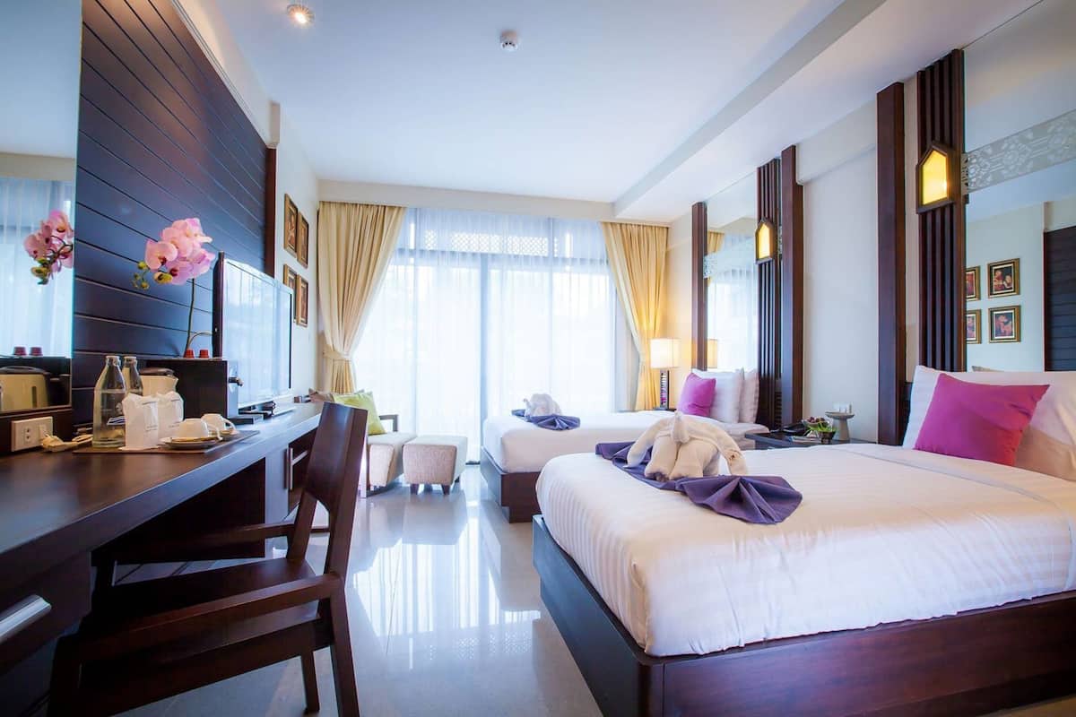 Una habitación de hotel con cama, escritorio, silla, una mesita y ventana con cortinas.