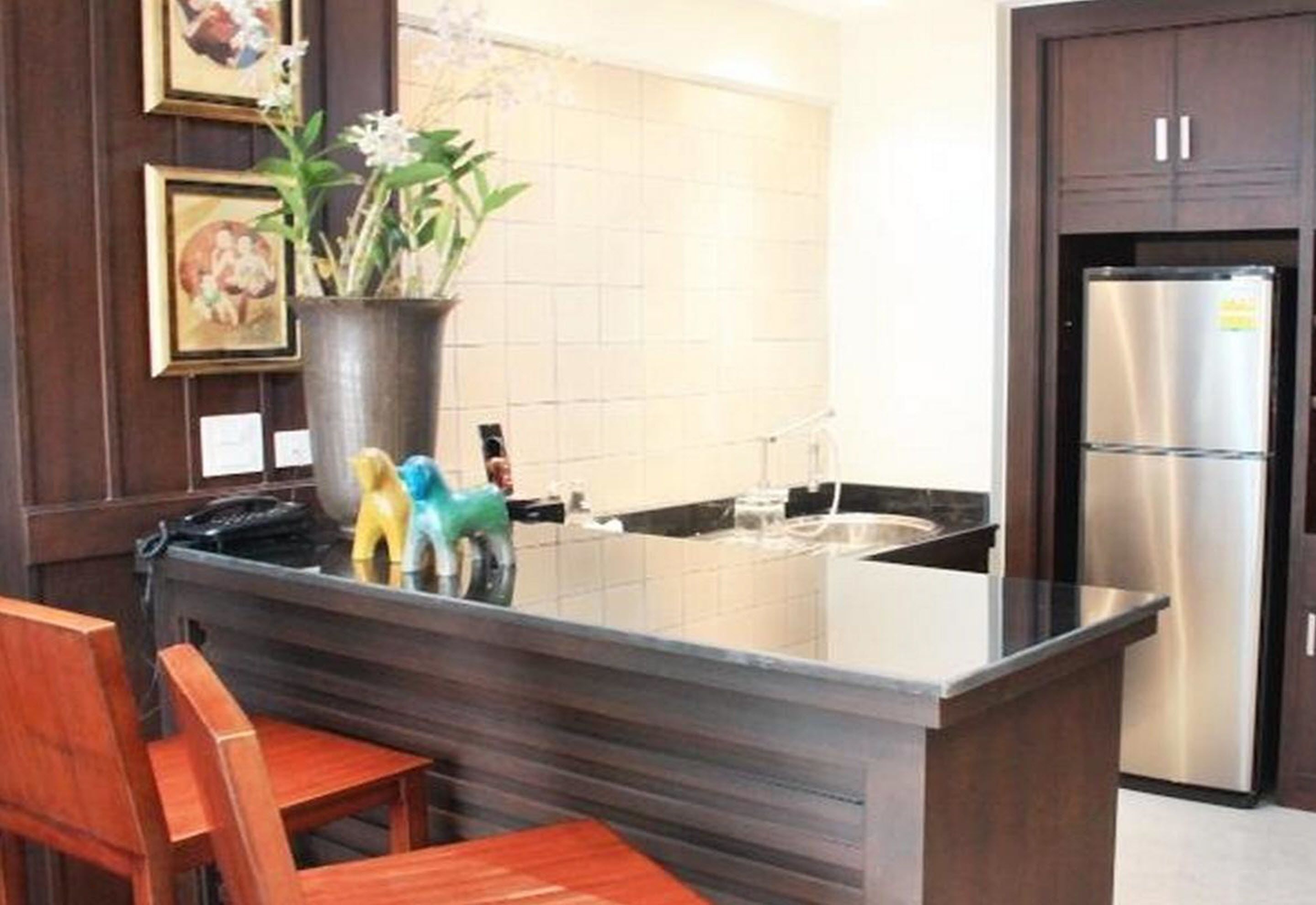 A kitchen with a central island, stainless steel refrigerator, wooden chairs, and framed artwork on the wall.