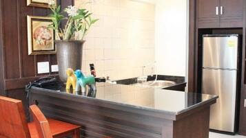 A kitchen with a central island, stainless steel refrigerator, wooden chairs, and framed artwork on the wall.