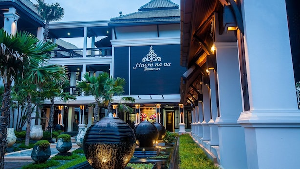 A hotel entrance with a sign reading "Huern na na" and a well-lit pathway with large decorative vases and palm trees. - Huern Na Na Boutique Hotel (Phrae)