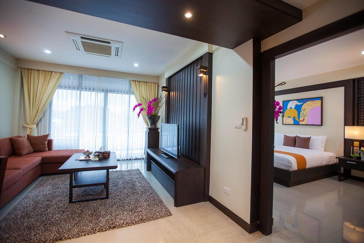 Una habitación de hotel moderna con sofá, una mesa de centro, televisor y cama.