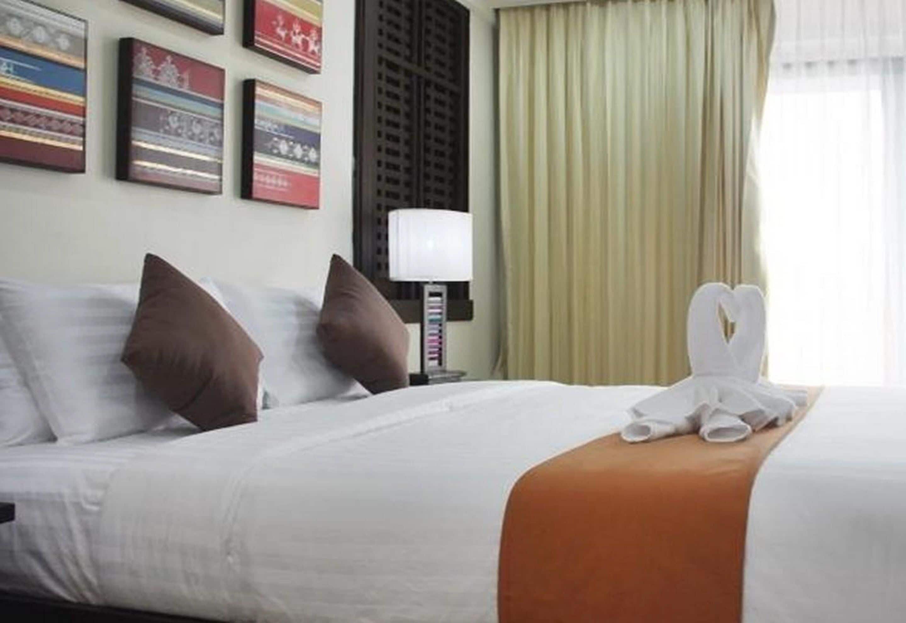 A hotel room with a neatly made bed, a lamp, and a window with curtains.