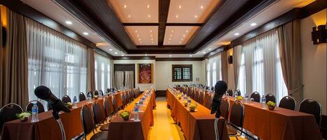 A conference room with long tables, microphones, and chairs, equipped with water bottles and small plants.