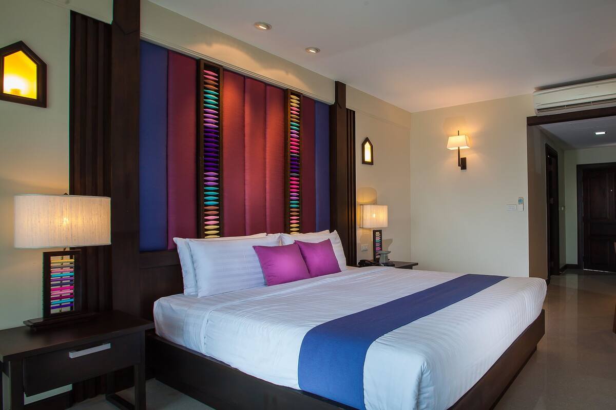 Una cama grande con detalles en azul, dos mesitas de noche con lámparas y un aplique de pared.
