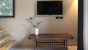 Una habitación moderna con una televisión de pantalla plana montada en la pared, un banco de madera y una maceta blanca con una planta.