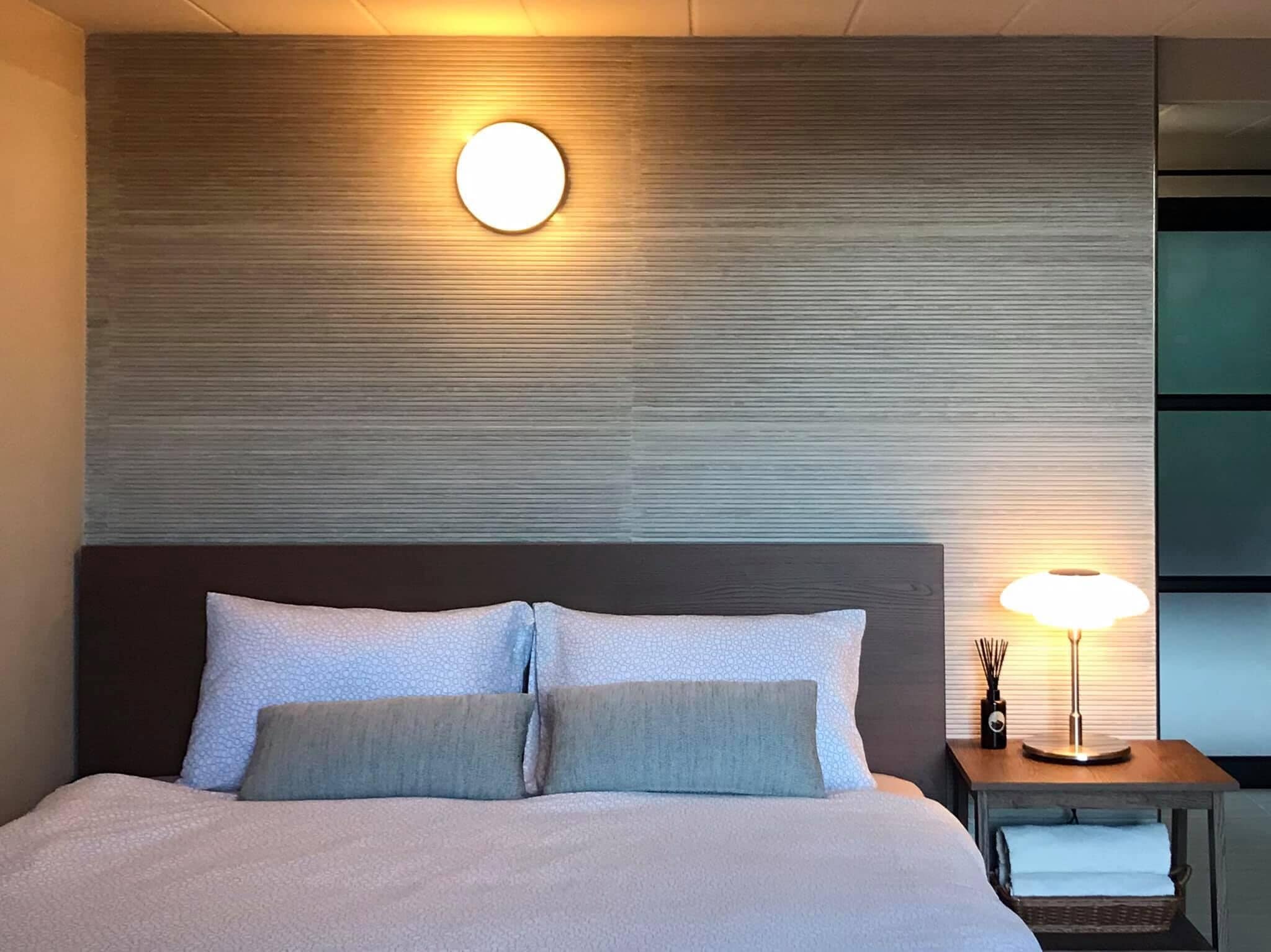A hotel room with a large bed, a round wall-mounted light, and a bedside table with a lamp.
