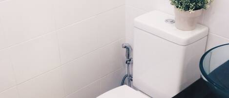 A white toilet with a small potted plant on top, a glass shower enclosure, and a wooden floor.