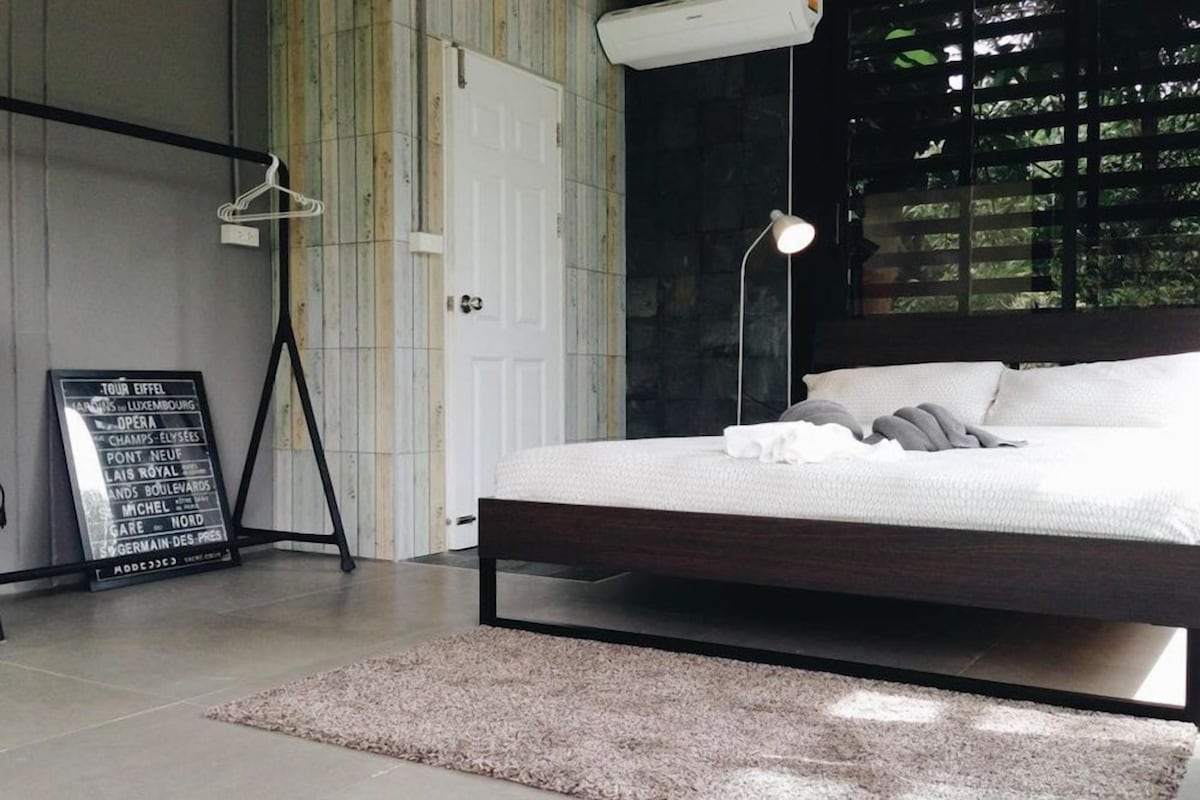 A modern bedroom with a bed, a hanging light, a blackboard with text, and a window with blinds.