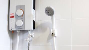 A bathroom with a white tiled wall, a Panasonic electric shower unit, and a handheld showerhead.