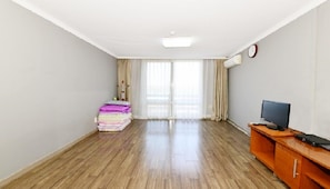 Habitación de hotel con piso de madera, un escritorio con una computadora, un televisor y una pila de toallas dobladas.