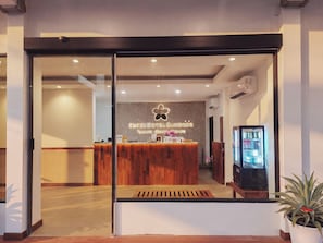 Un espace d’accueil d’hôtel avec un comptoir de réception en bois, un panneau fixé au mur et un distributeur automatique.