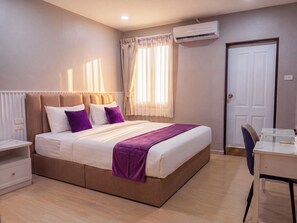 A bedroom with a bed, bedside table, chair, desk, and an air conditioning unit. - Excel Hotel Bangkok (Bangkok)