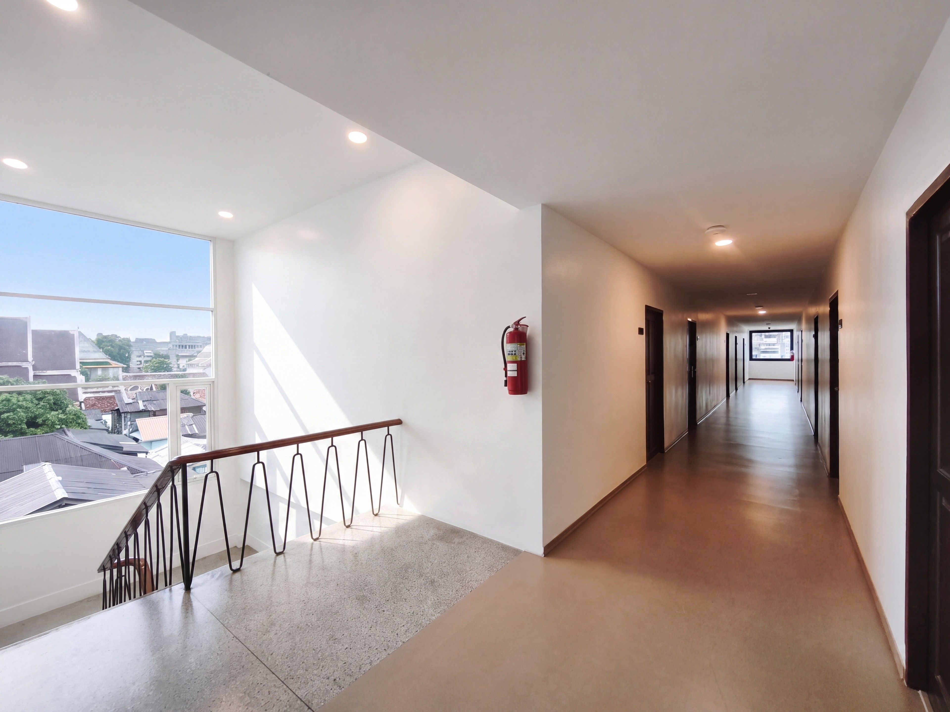Un pasillo de hotel con un extintor en la pared, una barandilla y vistas de la ciudad a través de amplios ventanales.