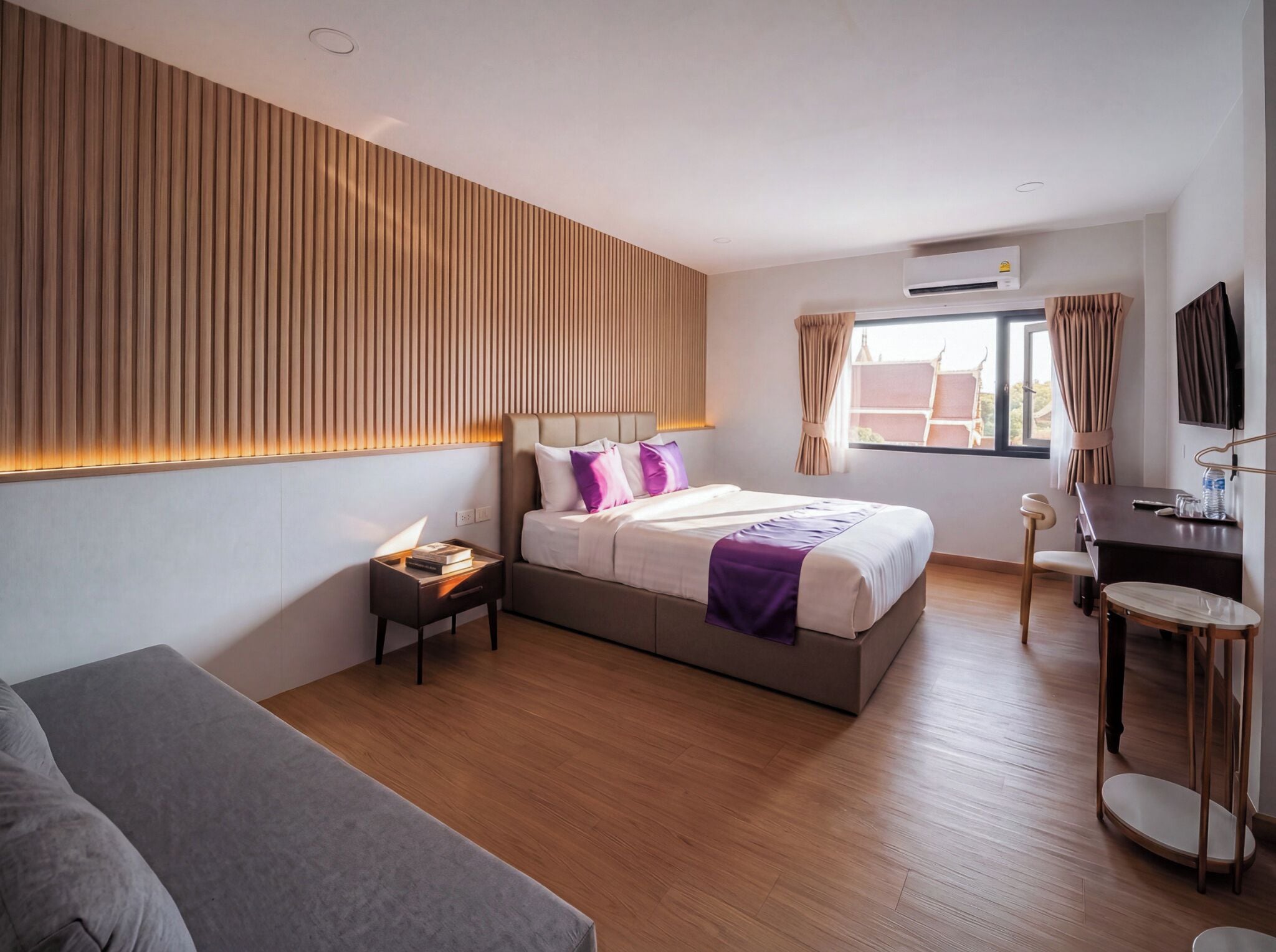 A modern hotel room with a bed, bedside table, and a desk with a chair.